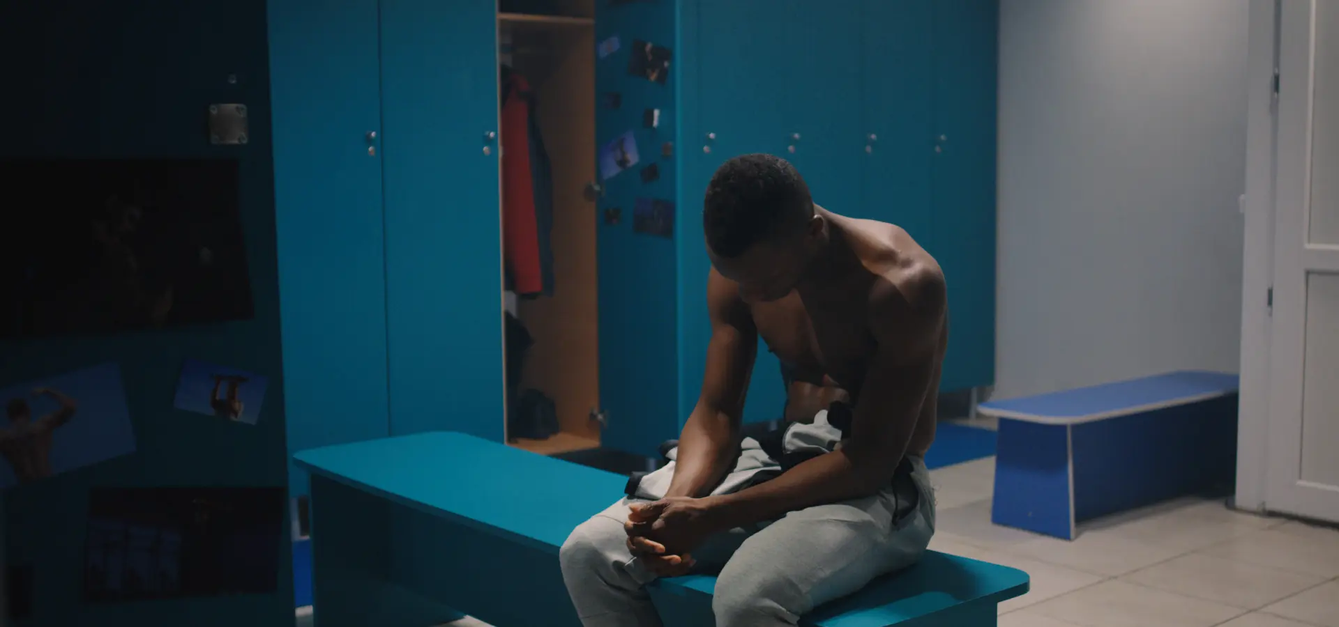 a young athlete who may have been hazed in an initiation for a sports team sits with his head down in a blue locker room