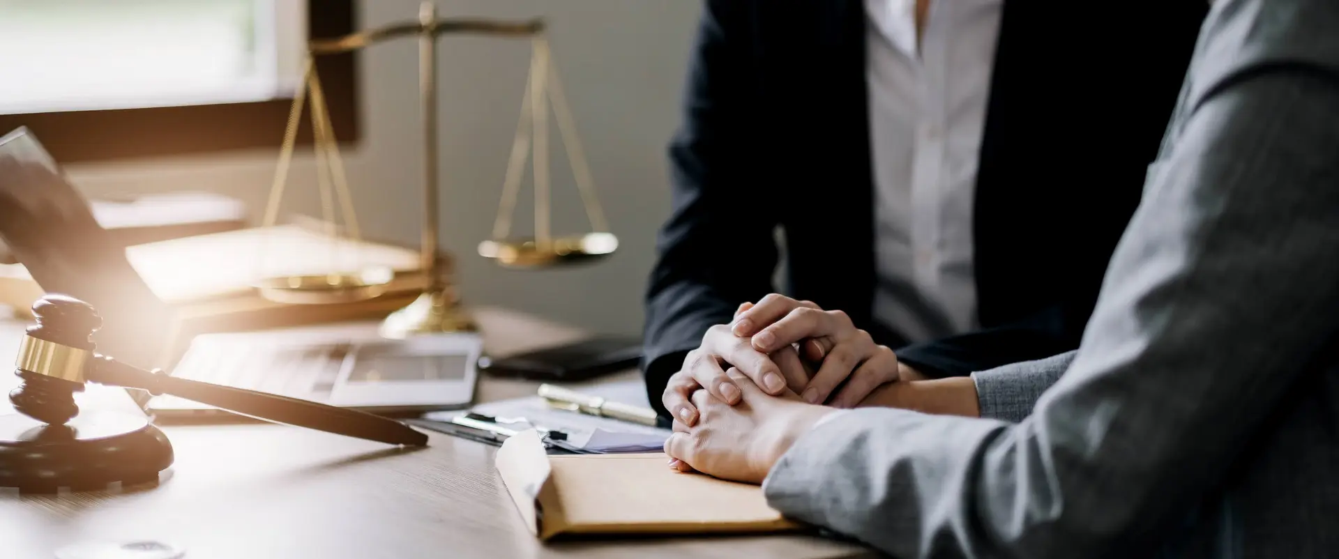 a lawyer sits in their offices and consoles a potential client as they work through their case. the scales of justice and a gavel sit on the desk.