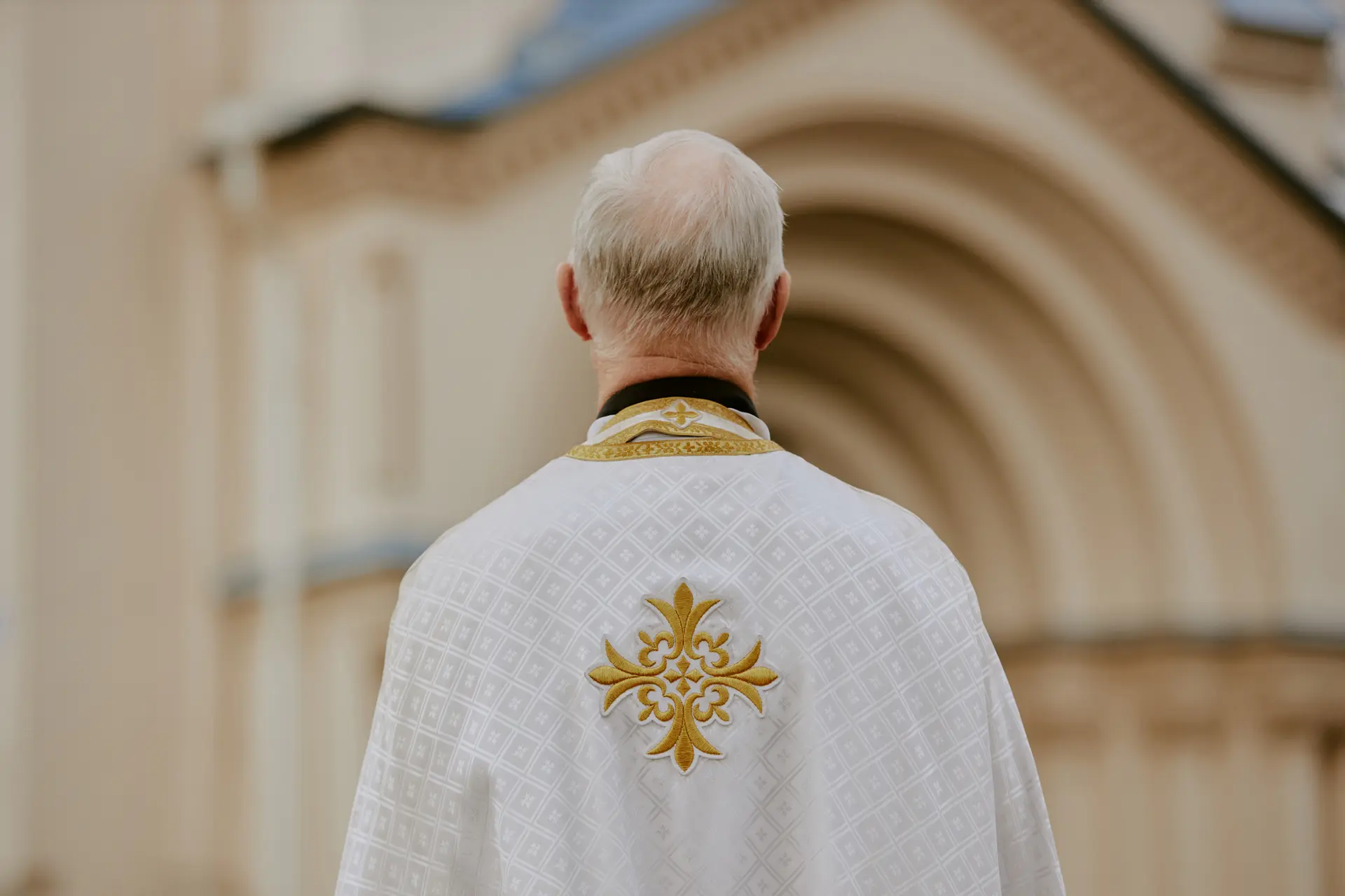 a priest is photographed from behind as he looks at a church in the distance