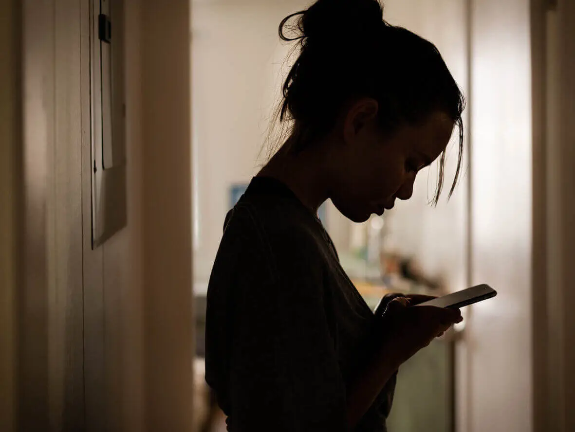 Silhouette of a sad female looking at her phone. Online harassment.