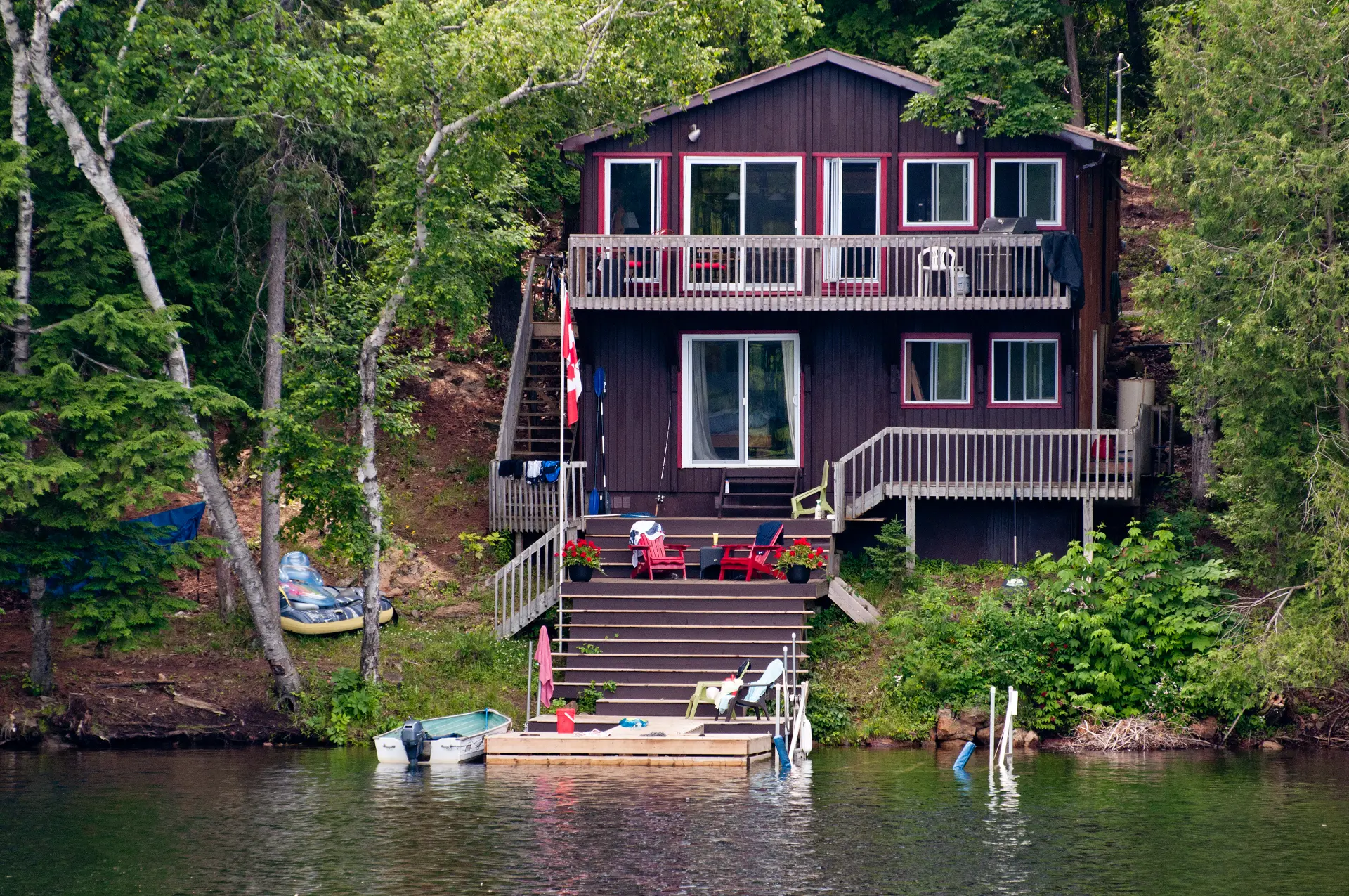 a brown lakefront cottage with red window panels and kayaks