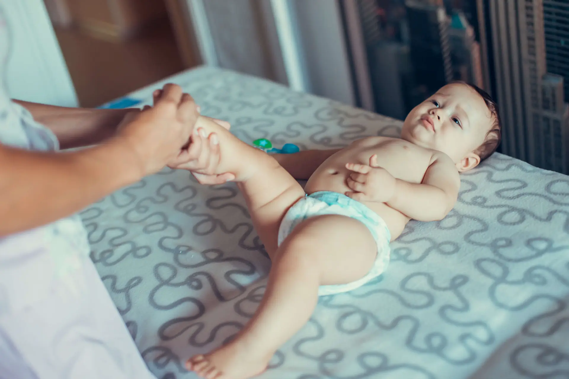 a baby in a diaper lays down on a patterned blanket while being examined by a doctor
