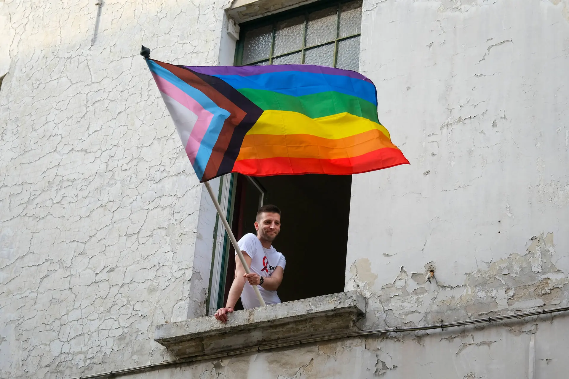 a person waves a LGBTQ2S  pride flag from a window in celebration and support of the LGBTQ2S  community