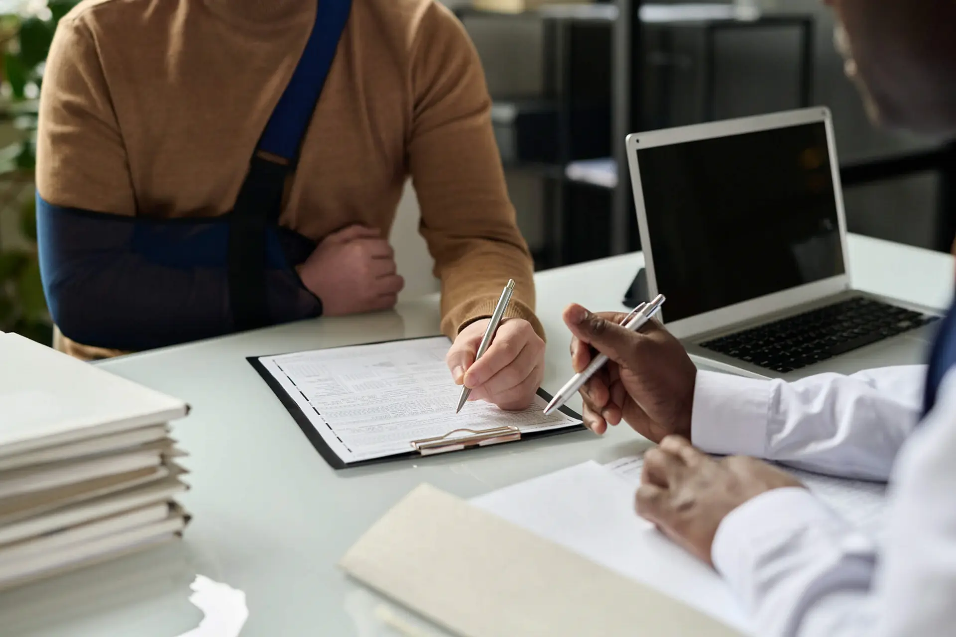 an injured person with their arm in a sling begins filling out forms with a personal injury lawyer