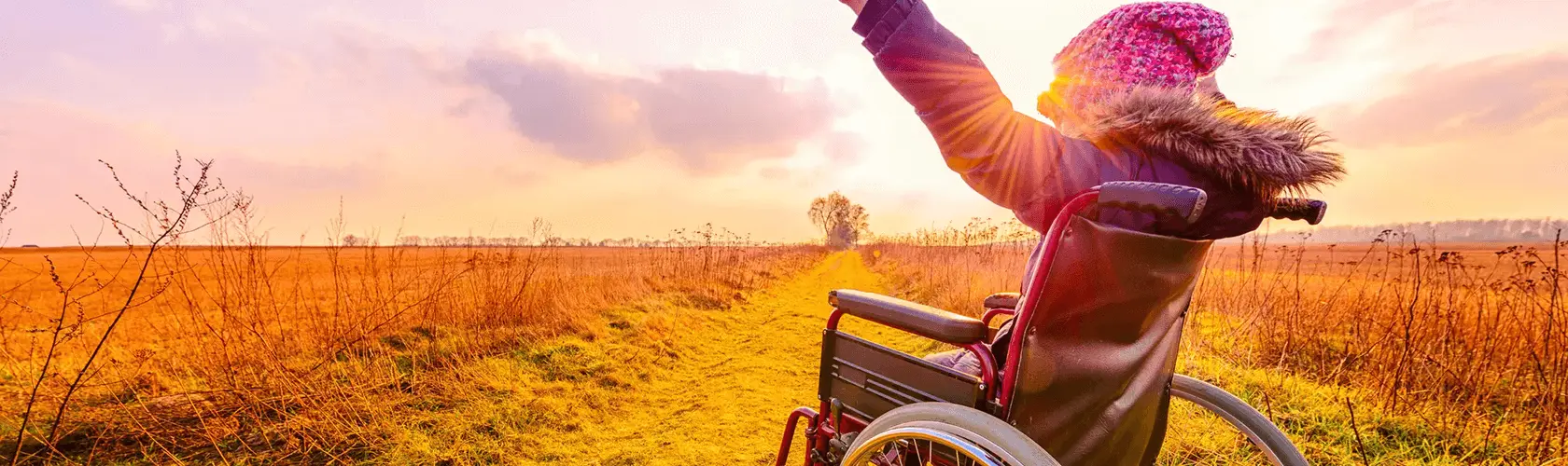 Child in wheelchair with arms up in a field