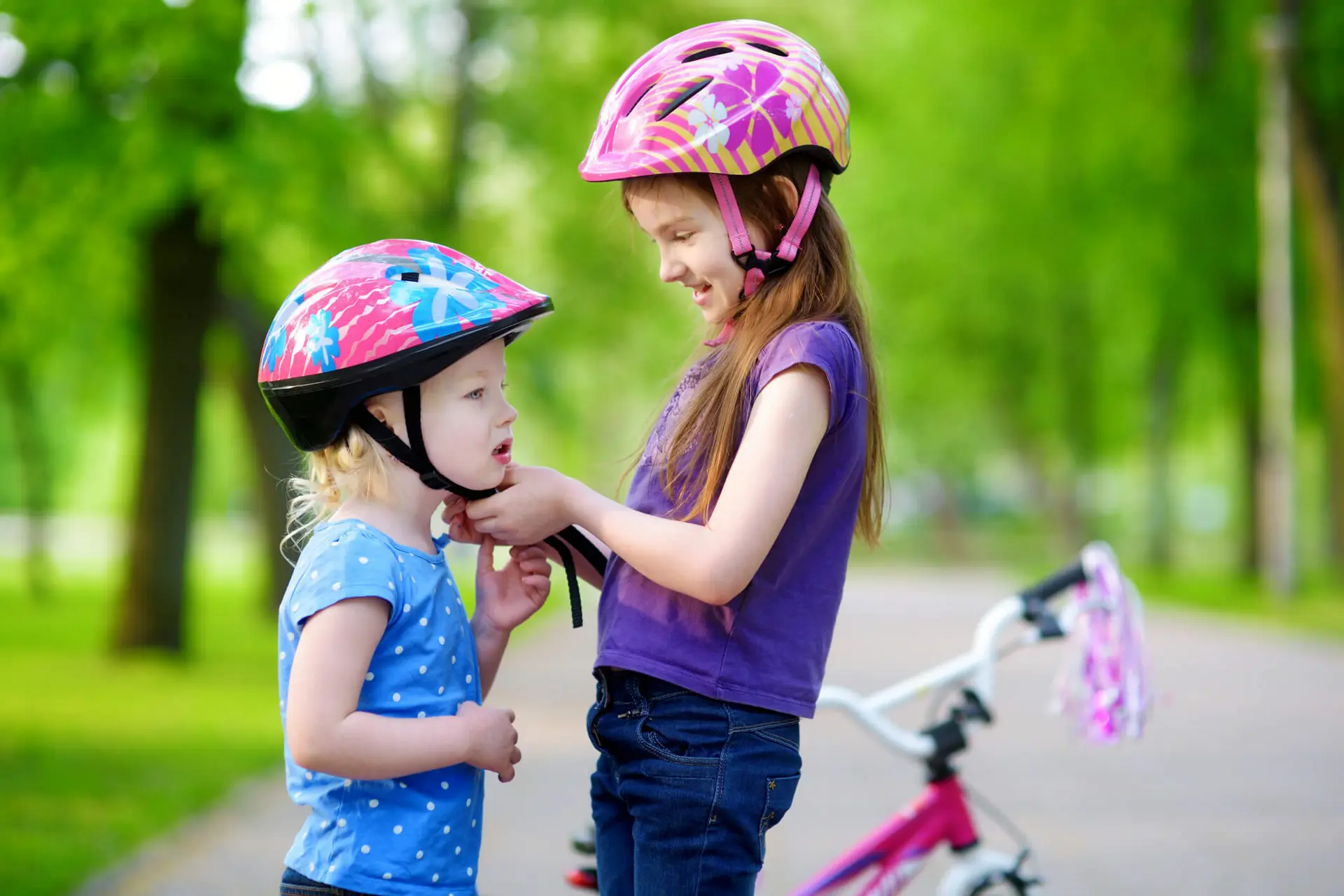 Big sister helping her little sister to put a bicycle helmet on